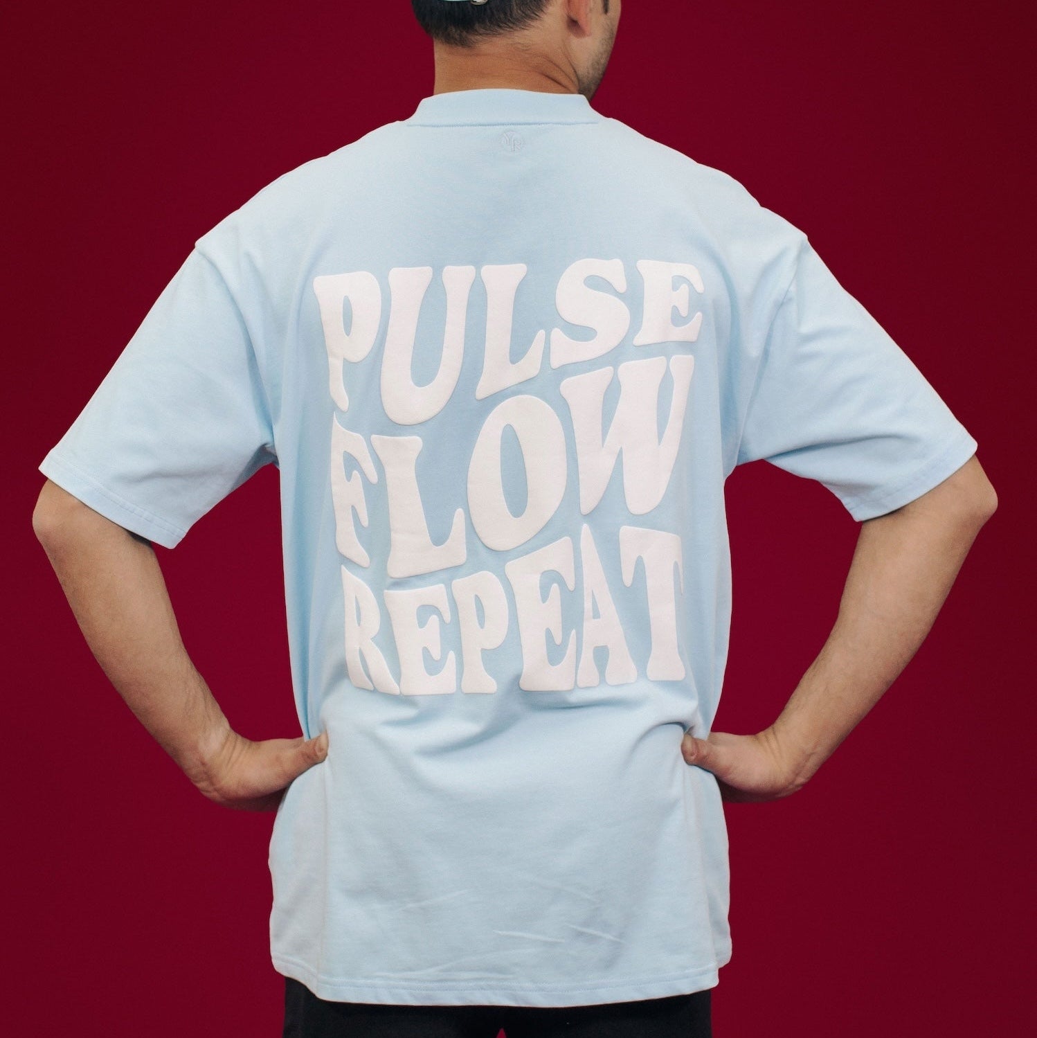 Person wearing a light blue t-shirt with 'Pulse Flow Repeat' text on the back against a red background